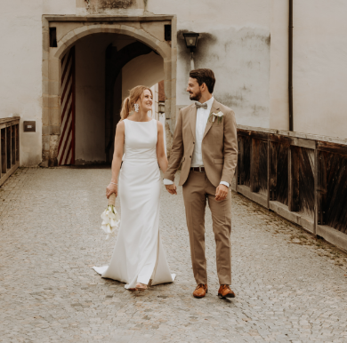 Brautpaar läuft händchenhaltend vor dem Torbogen eines Schlosses bei einem Hochzeitsfotoshooting