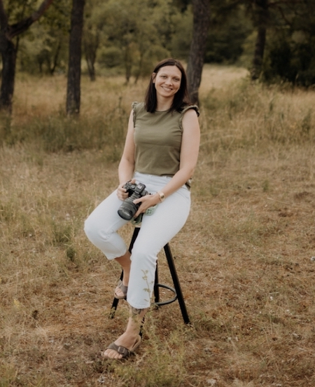 Fotografin Steffi Mertens sitzt auf einem Hocker in einem Wald und hält ihre Kamera in der Hand